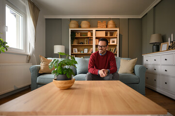 Smiling young businessman with hands clasped sitting on sofa and looking away in living room