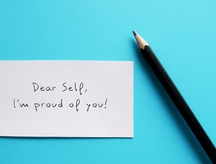 White paper on blue background with handwritten text DEAR SELF , I'M PROUD OF YOU self-love affirmation or self awareness to boost confidence