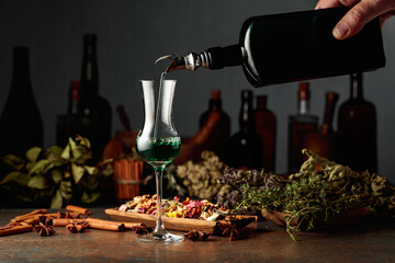 Green herbal liquor is poured from a vintage bottle into a glass.