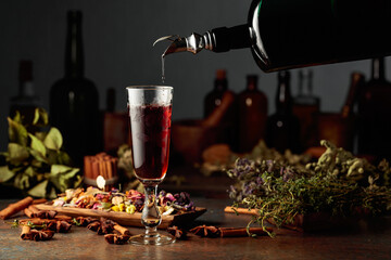 Brown herbal liquor or balm is poured from a vintage bottle into a glass.