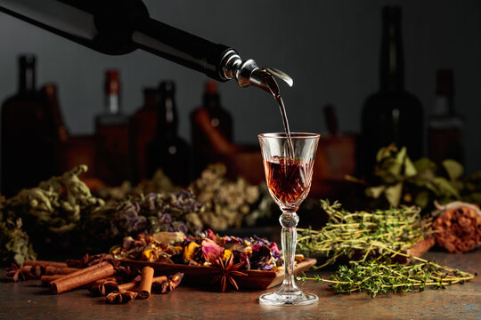 Brown Herbal Liquor Or Balm Is Poured From A Vintage Bottle Into A Glass.