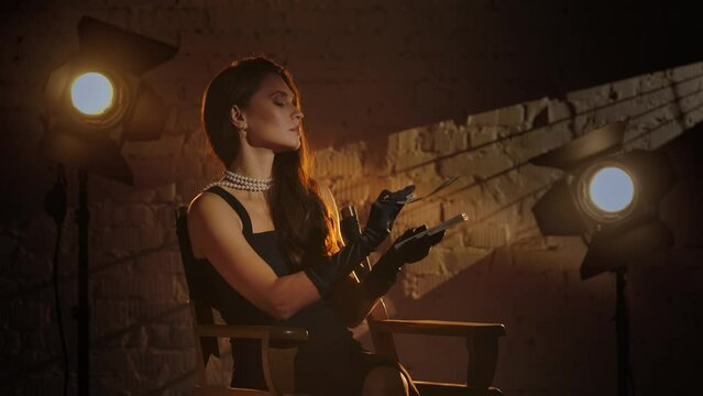 Woman in black dress sitting on a director's chair, holding money and counting it, throwing paper bills in the air. Slow motion.
