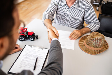 Farmer at tractor dealership signing contract and shaking hands with sales manager after purchasing agricultural machines and equipment.