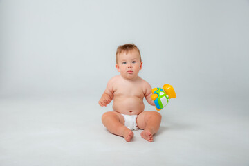 Fototapeta na wymiar Portrait of a little toddler boy, a baby in a diaper happily sitting playing with a toy car isolated on a white studio background. The concept of childhood, motherhood, life, birth. Place for text