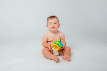 Fototapeta na wymiar Portrait of a little toddler boy, a baby in a diaper happily sitting playing with a toy car isolated on a white studio background. The concept of childhood, motherhood, life, birth. Place for text
