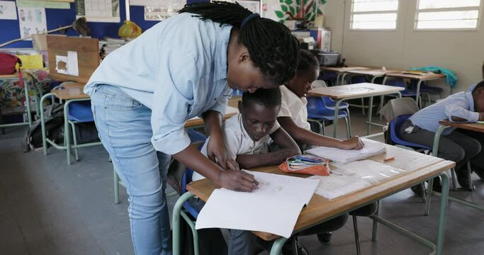 Close-up. Black African female teacher standing and assisting African children with a drawing at their desk in a classroom in Africa