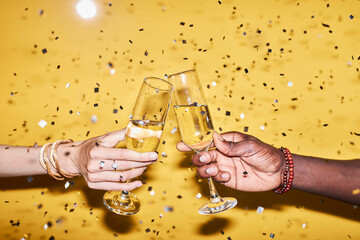 Closeup of two hands clinking champagne glasses against vibrant yellow background with confetti - obrazy, fototapety, plakaty