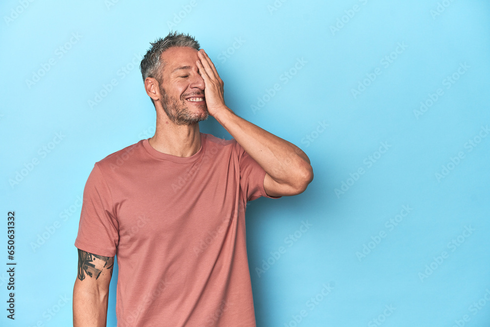 Wall mural Middle-aged caucasian man on blue backdrop laughing happy, carefree, natural emotion.