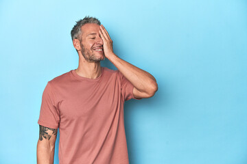 Middle-aged caucasian man on blue backdrop laughing happy, carefree, natural emotion.