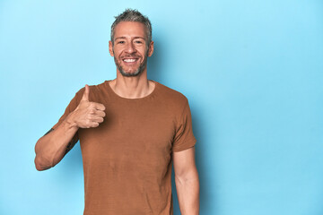 Middle-aged caucasian man on blue backdrop smiling and raising thumb up