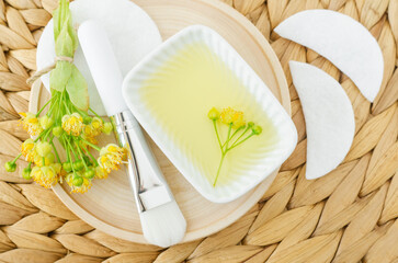 Small bowl with homemade linden (tilia, basswood, lime tree) face toner with linden flowers and make-up brush. Natural beauty treatment and spa recipe.