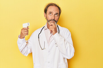 Doctor holding infrared thermometer in studio looking sideways with doubtful and skeptical...