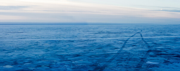 Frozen big lake in winter, path on ice, traces from hovercraft. Winter arctic tale on sunset, panoramic view - 650637333