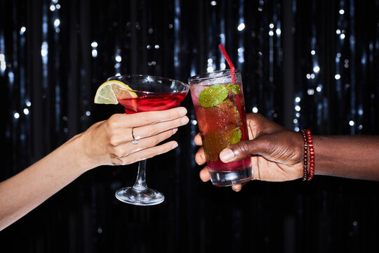 Close up of two people holding cocktails against glittering party background, copy space