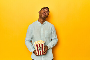African American man with popcorn, yellow studio, dreaming of achieving goals and purposes