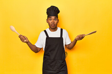 African American cook holding wooden spoon and fork in a yellow studio