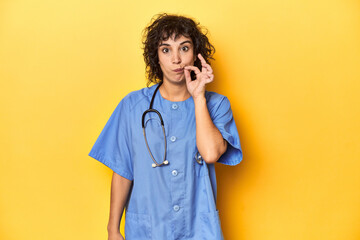 Curly-haired Caucasian woman nurse on yellow studio with fingers on lips keeping a secret.