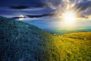 green grass on hillside meadow in high mountains under the cloudy blue sky with sun and moon at twilight. day and night time change concept. mysterious countryside scenery in morning light