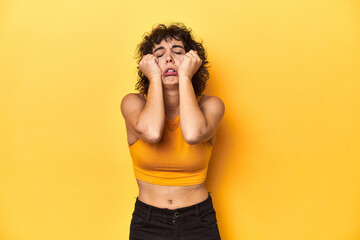Fototapeta na wymiar Curly-haired Caucasian woman in yellow top crying, unhappy with something, agony and confusion concept.