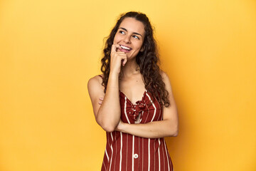 Young Caucasian woman, yellow studio background, relaxed thinking about something looking at a copy space.