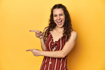 Young Caucasian woman, yellow studio background, pointing with forefingers to a copy space, expressing excitement and desire.
