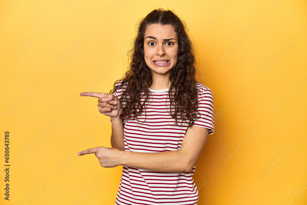 Wall mural young caucasian woman, yellow studio background, shocked pointing with index fingers to a copy space