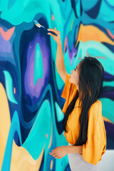 Female street artist painting colorful graffiti with paintbrushes on wall