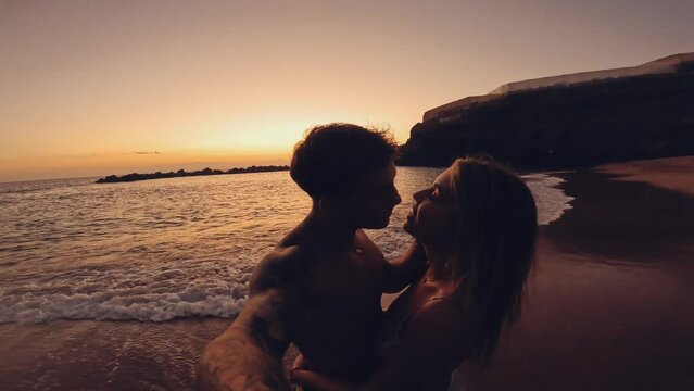 Couple of two young millennials people kissing and hugging together at the beach having fun and enjoying summertime with sunset at the background. Romantic moment on vacation