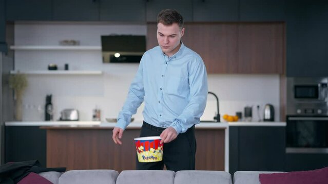 Tired young man taking off elegant jacket taking popcorn looking away thinking. Portrait of fatigue Caucasian freelancer businessman at the end of week at home indoors