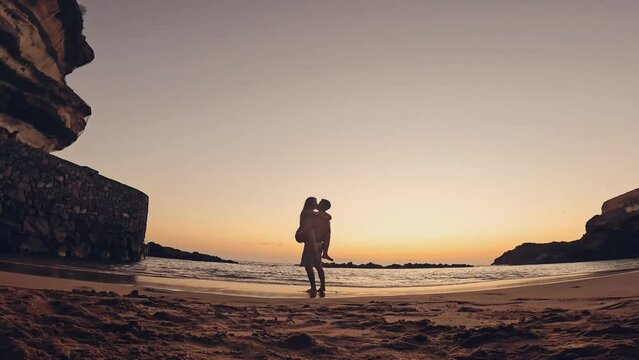 One happy and cute woman running to her boyfriend in love at sunset on the sand of the beach. Happy couple of millennials teenagers enjoying together. Young man holding girlfriend on his arms
