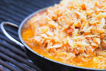 Country style dinner cooked on fire, barbecue. Stewed cabbage in a frying pan, bigos