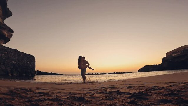 One happy and cute woman running to her boyfriend in love at sunset on the sand of the beach. Happy couple of millennials teenagers enjoying together. Young man holding girlfriend on his arms
