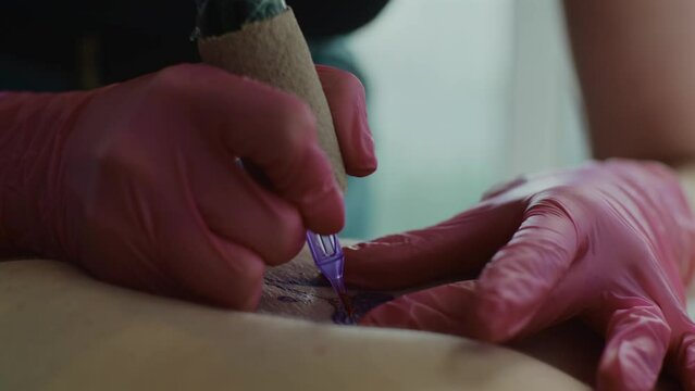 Tattoo master hands work at tattoo salon. Professional tattooist creating tattooing pattern on client's skin. Close up