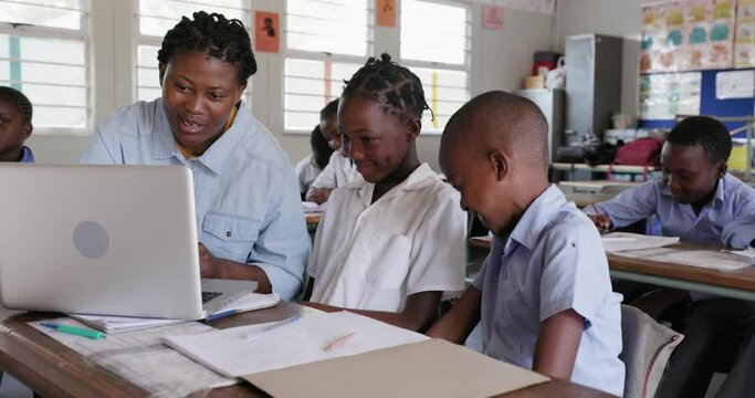 Close-up. Black African female teacher sitting and assisting African children at their desk with a task on a laptop in a classroom in Africa