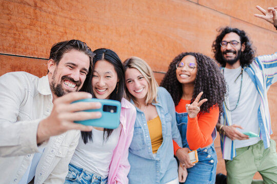 Group of young adult best friends taking a selfie portrait, smiling and laughing together. Cool friendly people having fun shooting a photo to share on the social media app using a cell phone outside