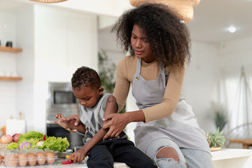 Multiracial mother and son have fun cooking meal together in kitchen at home. Young multiethnic woman and her little kid boy preparing healthy lunch with fresh vegetables. Motherhood enjoyment life.