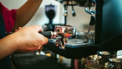 Fototapeta na wymiar Hands of barista holding portafilter to prepare coffee at automatic coffee machine in cafe