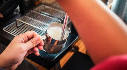 Fototapeta na wymiar Professional barista warming milk for cappuccino. hand of Barista using the coffee machine for coffee latte