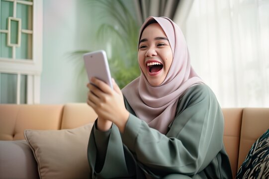 Energetic and Happy Asian Woman Wearing Hijab Getting Cellphone Notification, Excited and Engaged
