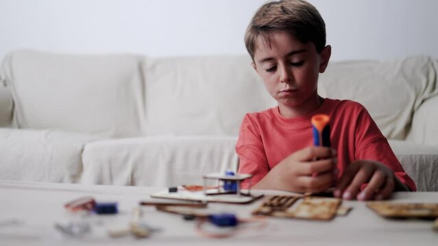 Latino kid building robotic toy machine inside home living room - Homeschool project, STEM science education