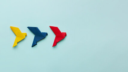 three paper origami pigeons yellow, blue and red in line to right on light blue background