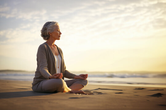 Elderly woman meditating on the beach. Sunset. Copy space. 