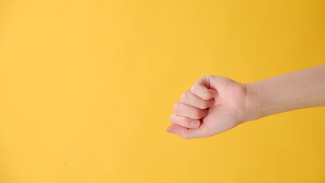 Vertical video of unrecognizable young caucasian woman knock knocking on camera, posing isolated over yellow studio background with copy space for promotion content or design. Hand gesture concept