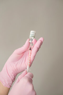 Hands of a cosmetologist doctor in pink gloves fill a syringe with disport drug, botulinum toxin for beauty injections on a gray background with copy space