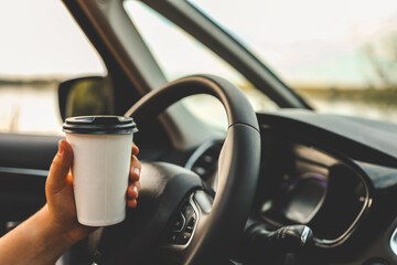 Paper cup with coffee in hand, traveling by car
