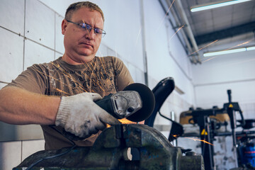 A master in glasses grinds a part clamped in a vice with a grinder