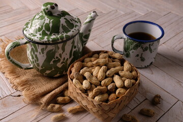 peanuts in a woven bamboo container on wooden table. Arachis hypogaea. a teapot and a cup of tea. tea time. 