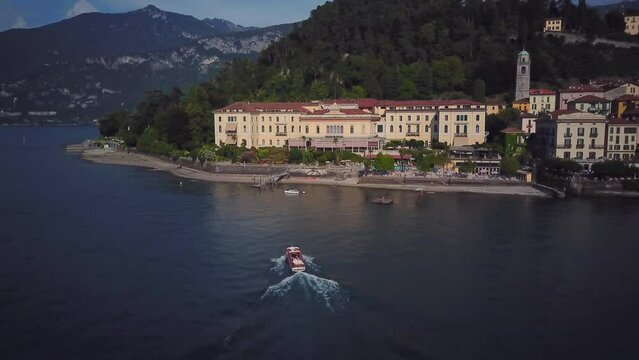 Drone Shot of Small Boat Sails Up to Villa. Yacht on Lake Como Moored to House. Aerial View of Yacht with a White Sail on Lake Como. Vacation in italy Concept