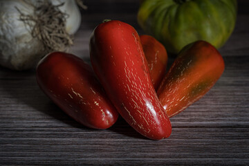 A close up of several ripe red jalapeno peppers with a green tomato and a head of garlic in the background. - 650687927