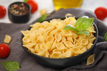 Uncooked dry conchiglie rigate pasta in a black bowl on an isolated white background.